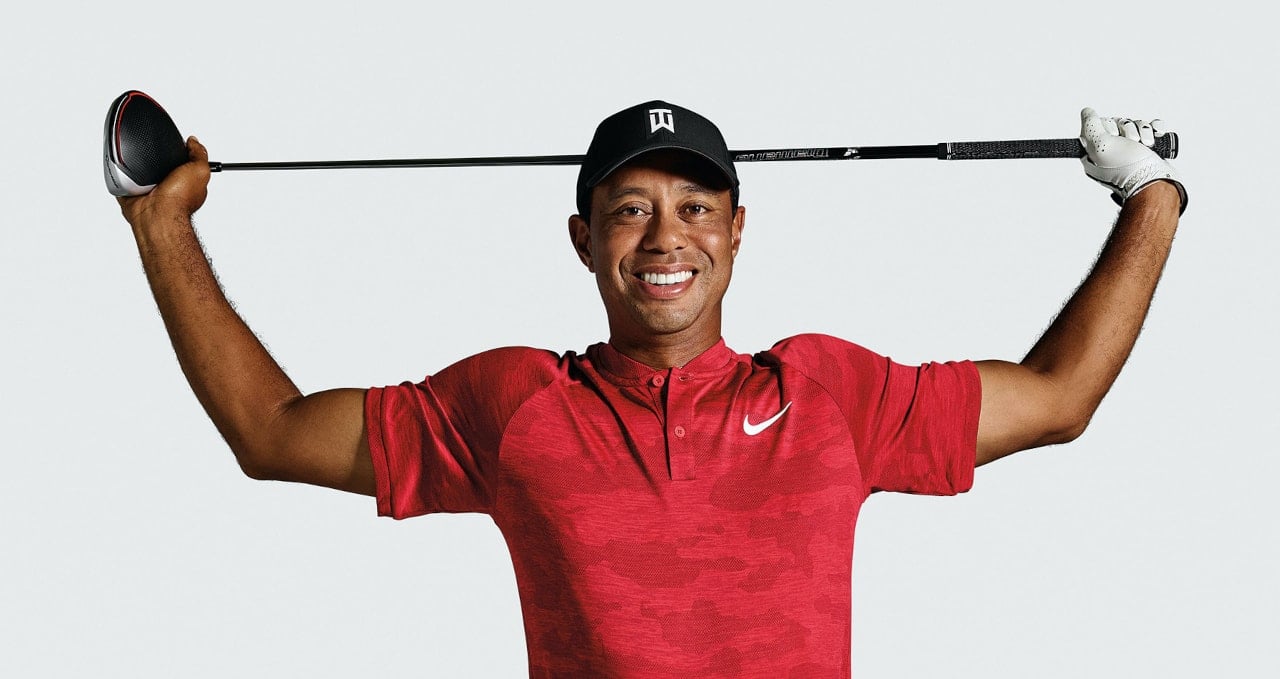 Tiger Woods in a red Nike golf shirt holding a gold club behind his head
